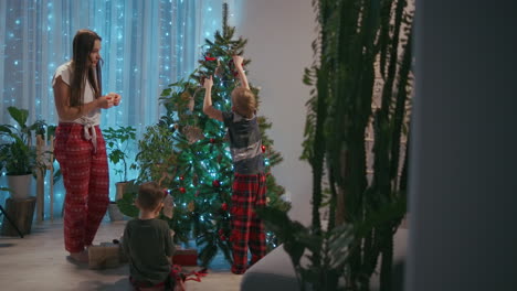 A-family-mother-and-two-children-decorate-a-Christmas-tree-with-toys-in-the-living-room-of-their-home.-Christmas-decorations-and-preparation-for-the-holiday.-High-quality-4k-footage